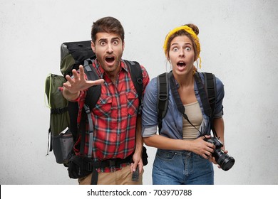 Studio shot of terrified shocked young man and woman travelers with backpacks and camera screaming, feeling frustrated, waving after departing train.Two tourists are worried after they missed flight