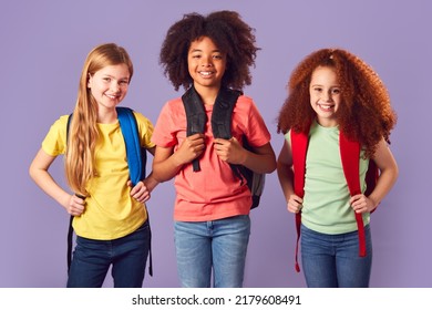 Studio Shot Of Three Children With Backpacks Going To School On Purple Background