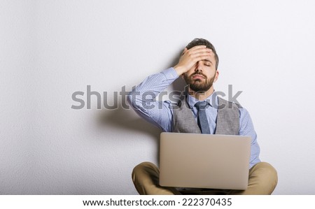 Studio shot of tired hipster businessman working on laptop