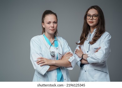 Studio Shot Of Two Female Doctors Dressed In Labcoats Posing With Crossed Arms.