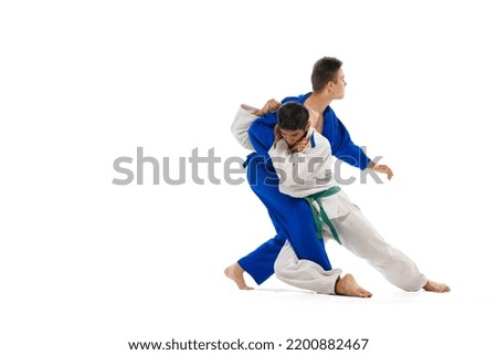 Studio shot of two men, professional judo athletes training isolated over white background. Sweeping hip throw. Concept of martial art, combat sport, health, strength, energy, fit. Copy space for ad