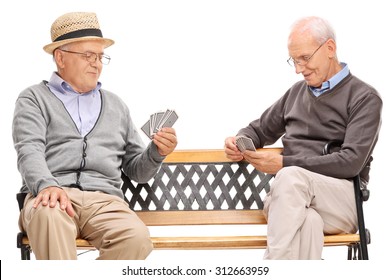 Studio Shot Of Two Older Men Playing Cards Seated On A Wooden Bench Isolated On White Background