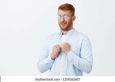 Studio Shot Of Weak And Silly Mature Redhead Guy In Transparent Glasses And Shirt, Raising Fists Uncertainly, Frowning And Gazing Worried And Intense At Camera, Scared Being Beaten Over Gray Wall