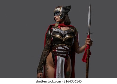Studio shot of wild female warrior from past with painted face holding spear isolated on grey background.