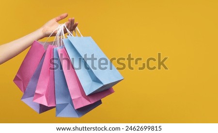Studio shot of woman hand holding a bunch of colorful paper shopping bags isolated over yellow background. Copy space for your text or logo.