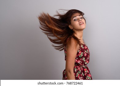 Studio shot of young beautiful Indian woman wearing dress while flipping hair against gray background