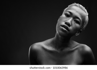 Studio shot of young beautiful rebellious Asian woman with short hair against gray background in black and white