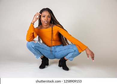 Studio Shot Of A Young Black Woman With Vintage Orange Top And Baggy Jeans Posing On A White Background Squatting