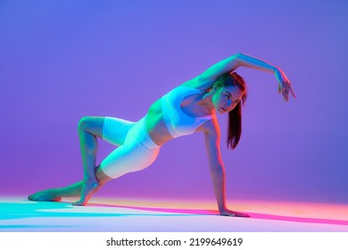 Studio shot young flexible girl in fitness sport uniform practicing isolated gradient pink  purple background in neon light  Modern sport  action  fitness  yoga  motion  youth concept 