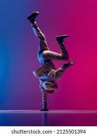 Studio shot of young flexible sportive man dancing breakdance in white outfit on gradient pink blue background. Concept of action, art, beauty, sport, youth. Dancer shows breakdance figures