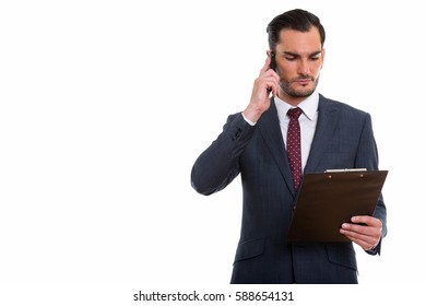 Studio shot of young handsome businessman looking at clipboard while talking on mobile phone
