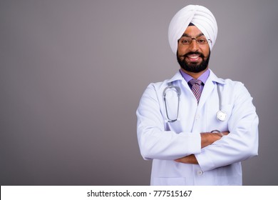 Studio shot of young handsome Indian Sikh man doctor against gray background