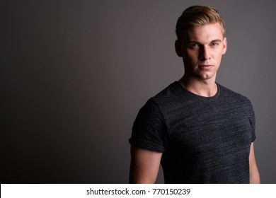 Studio shot of young handsome man with blond hair wearing gray shirt against gray background