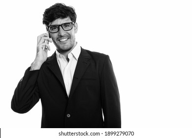 Studio shot of young happy Persian businessman smiling while talking on mobile phone
