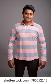 Studio Shot Of Young Indian Man Wearing Long Sleeve Striped Polo Shirt Against Gray Background