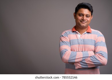 Studio Shot Of Young Indian Man Wearing Long Sleeve Striped Polo Shirt Against Gray Background