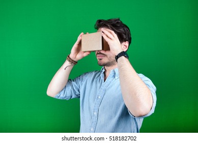 studio shot of a young, male model looking through cardboard virtual reality (VR) headset, isolated on green screen. - Powered by Shutterstock