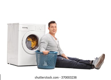 Studio Shot Of A Young Man Sitting By A Washing Machine And Doing Laundry Isolated On White Background