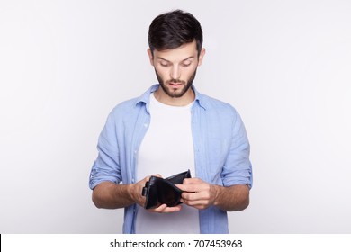 Studio shot of young man who counts the income,revenue or salary on the black leather wallet and found it almost empty. The crisis hits financial well-being of handsome Caucasian office manager.