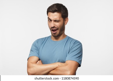 Studio Shot Of Young Man Winking While Flirting, Isolated On Gray Background