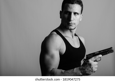 Studio Shot Of Young Muscular Persian Man Holding Gun And Thinking While Looking Back Against Gray Background