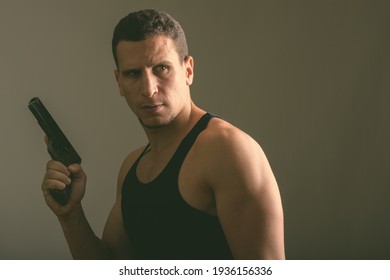 Studio Shot Of Young Muscular Persian Man Holding Gun While Thinking And Looking Back In Dark Room