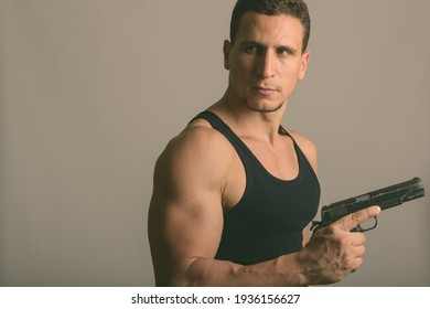 Studio Shot Of Young Muscular Persian Man Holding Gun And Thinking While Looking Back Against Gray Background