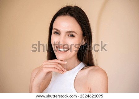 studio shot of young smiling woman with healthy radiant skin looking at camera and touching her chin. eyebrow lamination, skincare concept