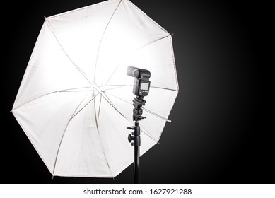 Studio stand with speedlight photo flash and white umbrella reflector, equipment in a photo studio.