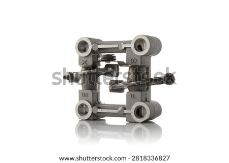 Studio three quarter perspective view of aluminum cylinder head rocker arm holder assembly featuring intake and exhaust valve rockers with adjustment screws, shaft springs, and cast bracket, shot on reflective white background showcasing four stroke engine valvetrain hardware.
