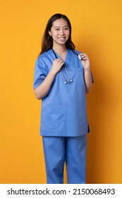 Studio vertical shot with orange background of a friendly asian female doctor in uniform