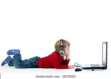 A Studio View Of A Young Preschool Boy, Laying On The Floor And Listening To Music Or A Video On A Laptop Computer.