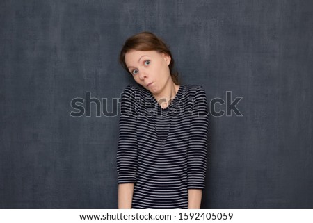 Studio waist-up portrait of surprised shocked dumbfounded girl wearing jumper, looking questioningly and with perplexity at camera, being unaware of how it happened, standing over gray background