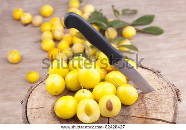 studio-shot of small\
yellow plums also known as mellow mirabelles, on a tree trunk. one\
is halved with a\
knife.