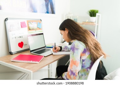Studious adolescent girl writing on a notebook and doing her homework. Smart teenage girl sitting on her bedroom desk and doing school work 
