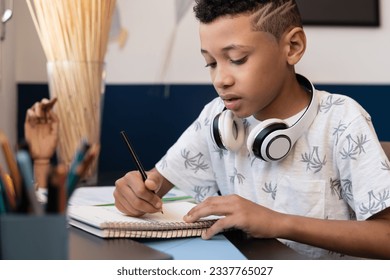 Studious boy writes in school notebook at desk in room