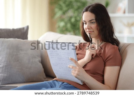 Studious student reading notes in a notebook and memorizing sitting on a couch at home