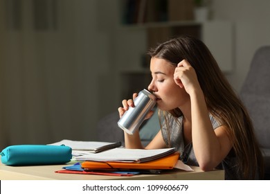 Studious teen studying drinking energy beverage while is studying in the night at home