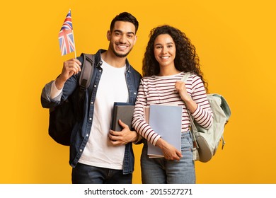 Study Abroad. Cheerful Young Arab Man And Woman With Backpacks Holding British Flag, Portrait Of Happy Smiling Students With Union Jack And Workbooks Over Yellow Studio Background, Copy Space - Shutterstock ID 2015527271