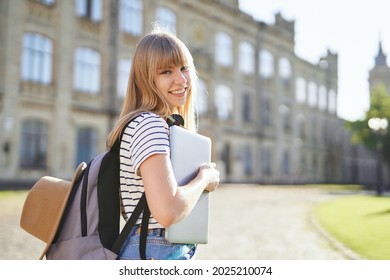 Study abroad, high school study or educational concept. Cute happy smiling blonde college or university student girl with backpack, hat and laptop in campus at summer. High quality image