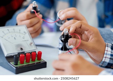 The study electrical circuit systems of students by experimenting with electrical connections using a small electric meter and a small flashlight bulb in physics science class, soft focus.