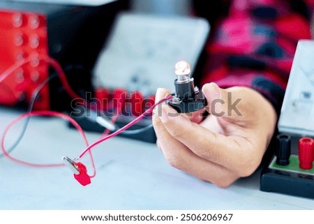 The study electrical circuit systems of students by experimenting with electrical connections using a small electric meter and a small flashlight bulb in physics science class, soft focus.