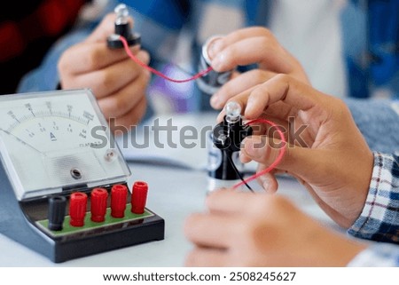 The study electrical circuit systems of students by experimenting with electrical connections using a small electric meter and a small flashlight bulb in physics science class, soft focus.