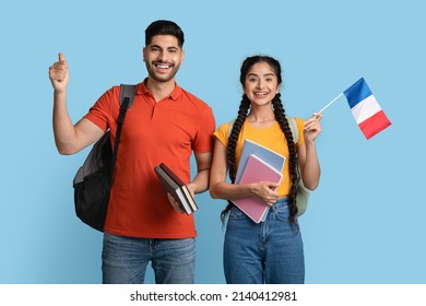 Study In France. Happy Arab Man And Woman Holding Workbooks And French Flag, Smiling Middle Eastern Students With Backpacks Posing Over Blue Studio Background, Recommending Study Abroad, Copy Space - Powered by Shutterstock