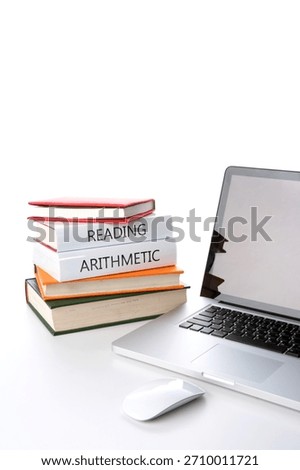 Study session setup featuring a laptop and stacked books on reading and arithmetic in a bright workspace