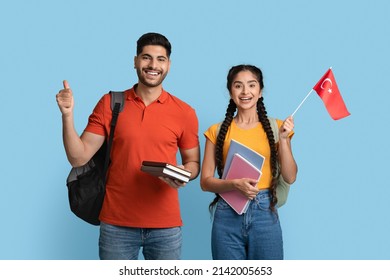 Study In Turkey. Happy Arab Student Couple With Workbooks Holding Turkish Flag And Gesturing Thumb Up, Middle Eastern Man And Woman Advertising International Education, Blue Background, Copy Space