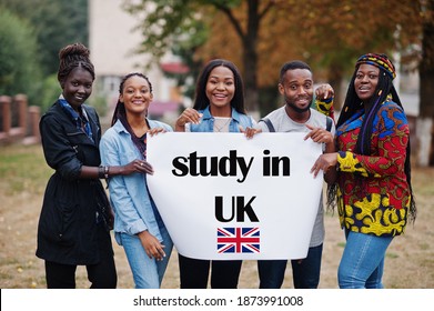 Study In UK. Group Of Five African College Students On Campus At University Yard Hold White Blank. Abroad Countries For Student Concept.