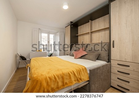 Study with wardrobe with folding bed and folding sofa and white folding dining table with matching chairs next to balcony with white wooden shutters Foto stock © 