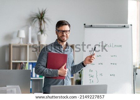 Studying English online. Cheerful mature male teacher giving online foreign language lesson, using computer and explaining grammar to remote students on web