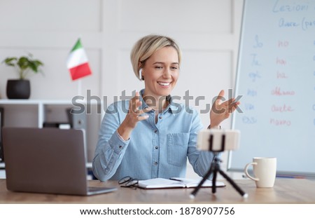 Studying foreign languages remotely. Cheerful female tutor teaching Italian on web, conducting online lesson on smartphone. Happy young teacher giving lecture on internet
